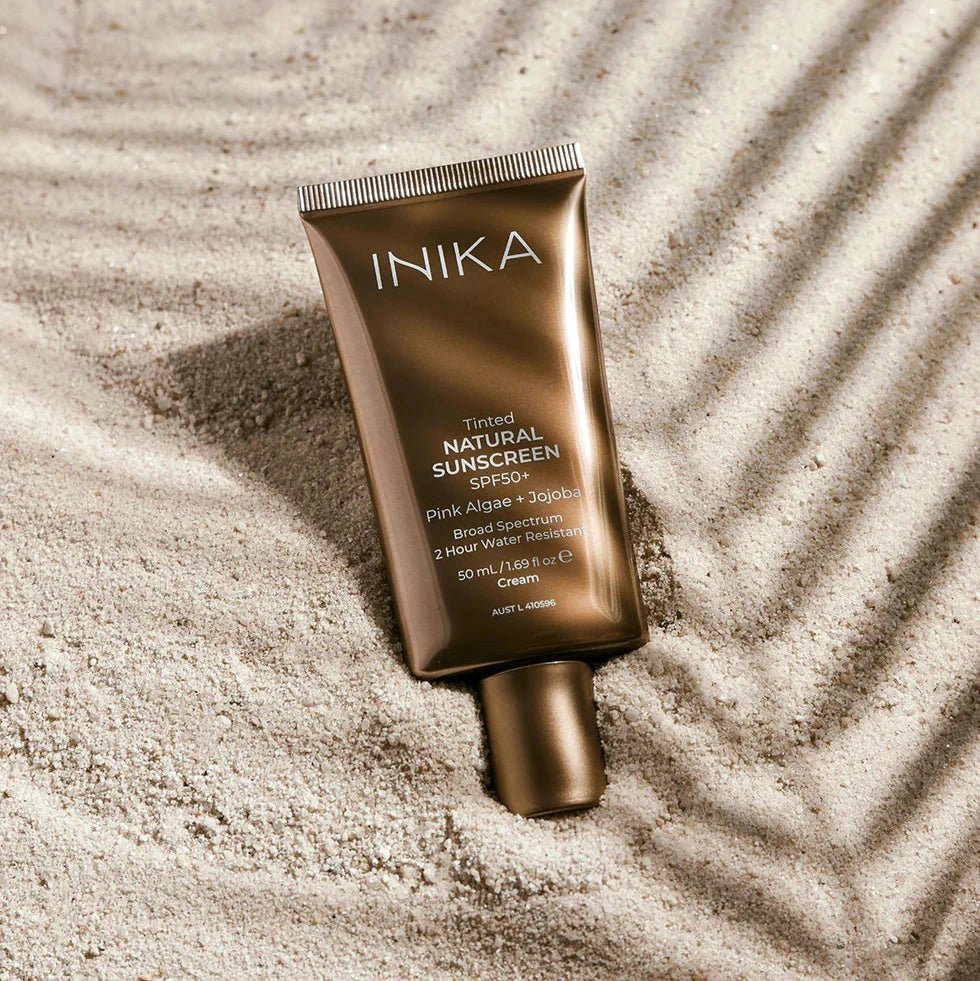 Inika Tinted Natural Sunscreen SPF50+ liegend im Sand.
