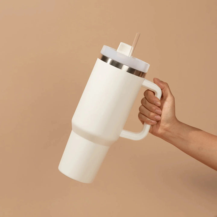 Eine Hand hält einen cremefarbenen Tumbler / Thermobecher von Sweet Water Decor vor hellem Hintergrund.