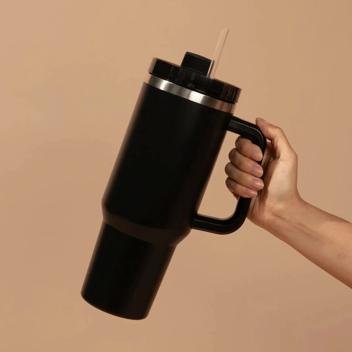 Eine Hand hält einen schwarzen Tumbler / Thermobecher von Sweet Water Decor vor hellem Hintergrund.