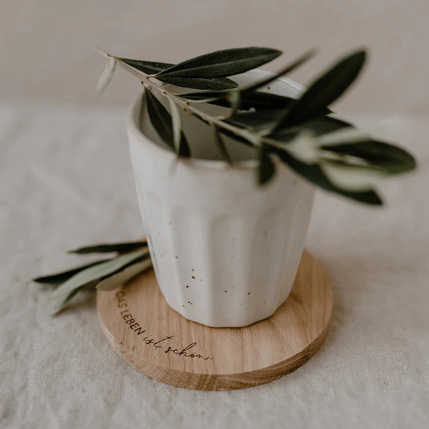 Untersetzer "DAS LEBEN ist schön" aus Eichenholz, darauf eine Tasse und einem Olivenzweig.