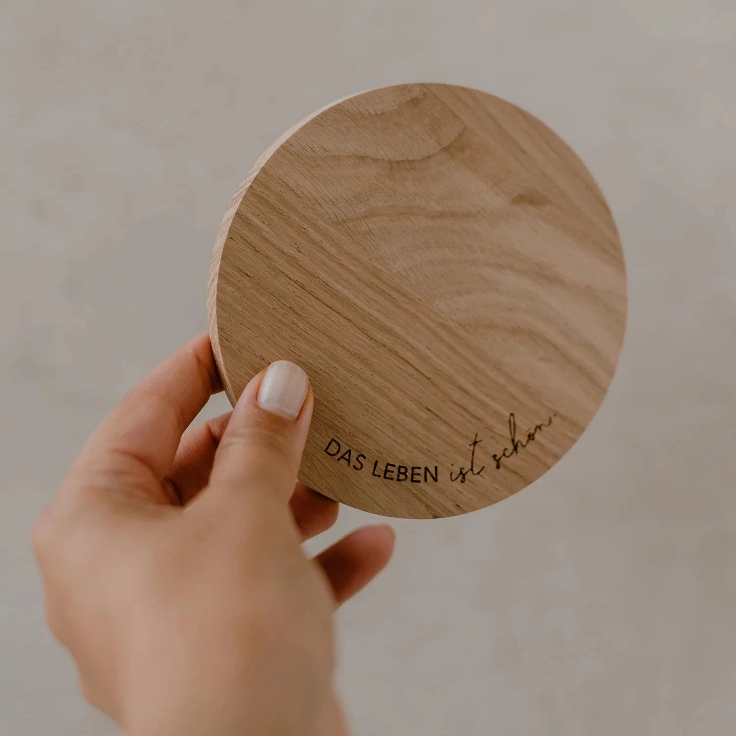 Untersetzer "DAS LEBEN ist schön" aus Eichenholz wird von einer Hand hochgehalten.