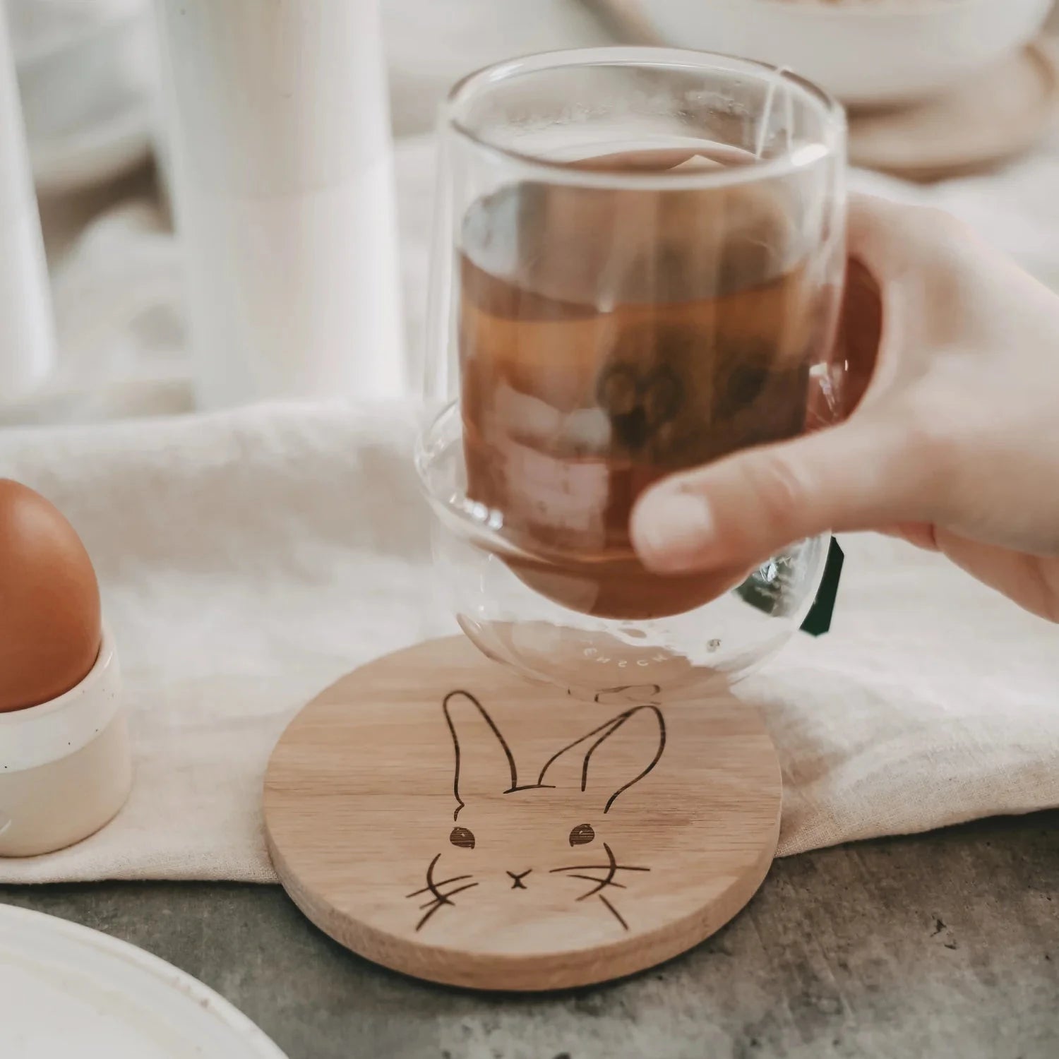 Untersetzer "Hase von Eulenschnitt, darüber wir ein Teelas von einer Hand gehalten.