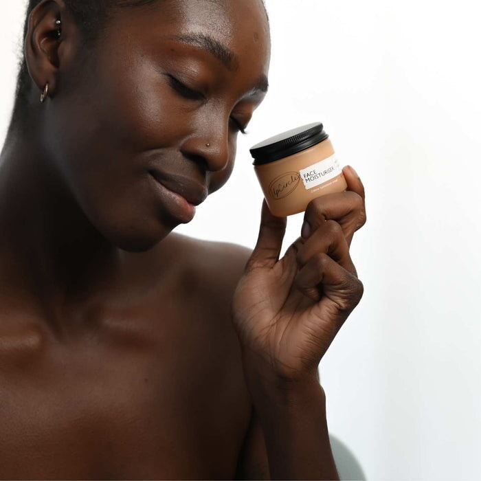 Model hält den geschlossenen Tiegel in der rechten Hand vor weißer Wand