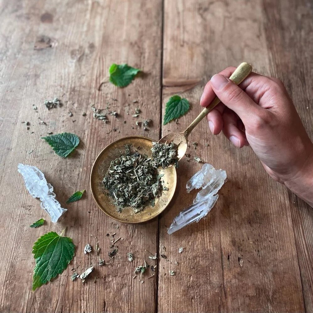 Loser Tee liegt in einer Messingschale und auf einem Messinglöffel, beides auf einem Hollzuntergrund.