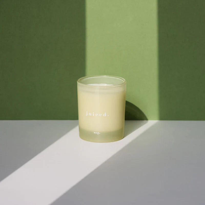 Kerze juiced von wxy. in cremefarbenem Glas vor grünem Hintergrund, angeleuchtet.