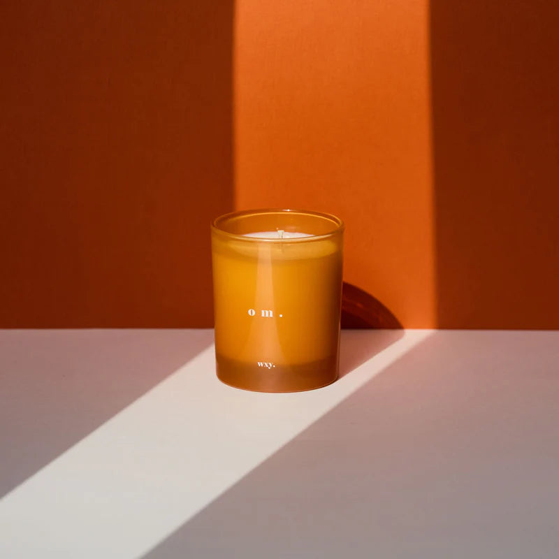 Kerze om von wxy. in orangenem Glas, vor angangenem Hintergrund, angeleuchtet.