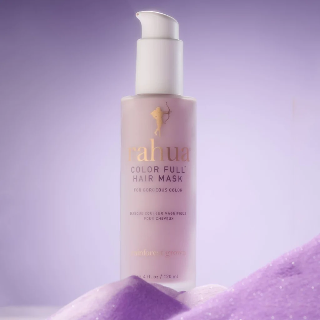 Strahlende Rahua Color Full Hair Mask Flasche vor lilafarbenem Hintergrund, steht auf lilafarbenem Glitzerpulver.