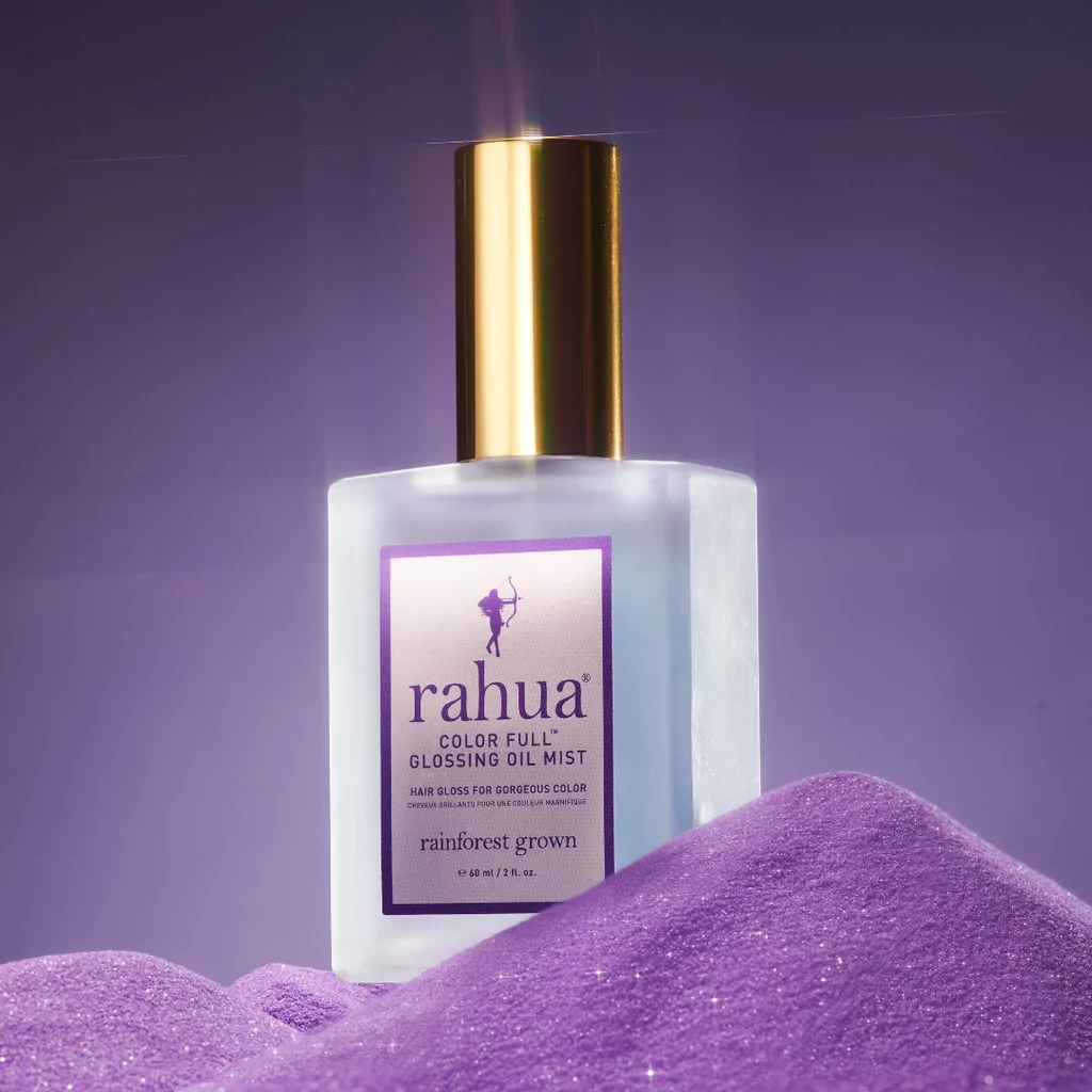 Strahlende Rahua Color Full Glossing Oil Mist Flasche vor lilafarbenem Hintergrund, steht auf lilafarbenem Glitzerpulver. North Glow