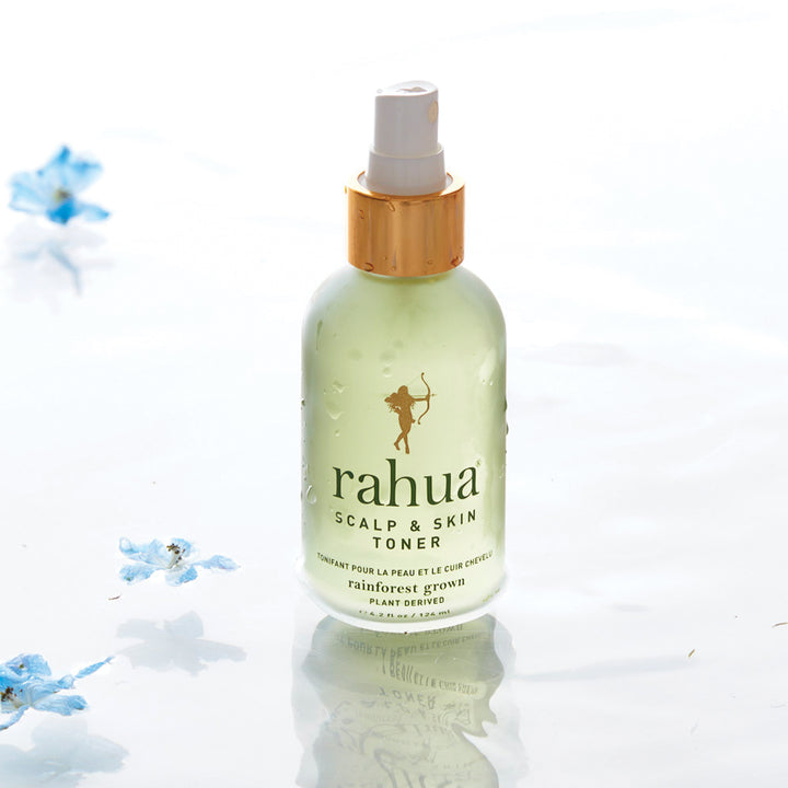 Rahua Scalp & Skin Toner Flasche steht im Wasser vor hellem Hintergrund, Blütenblätter schwimmen drumherum..