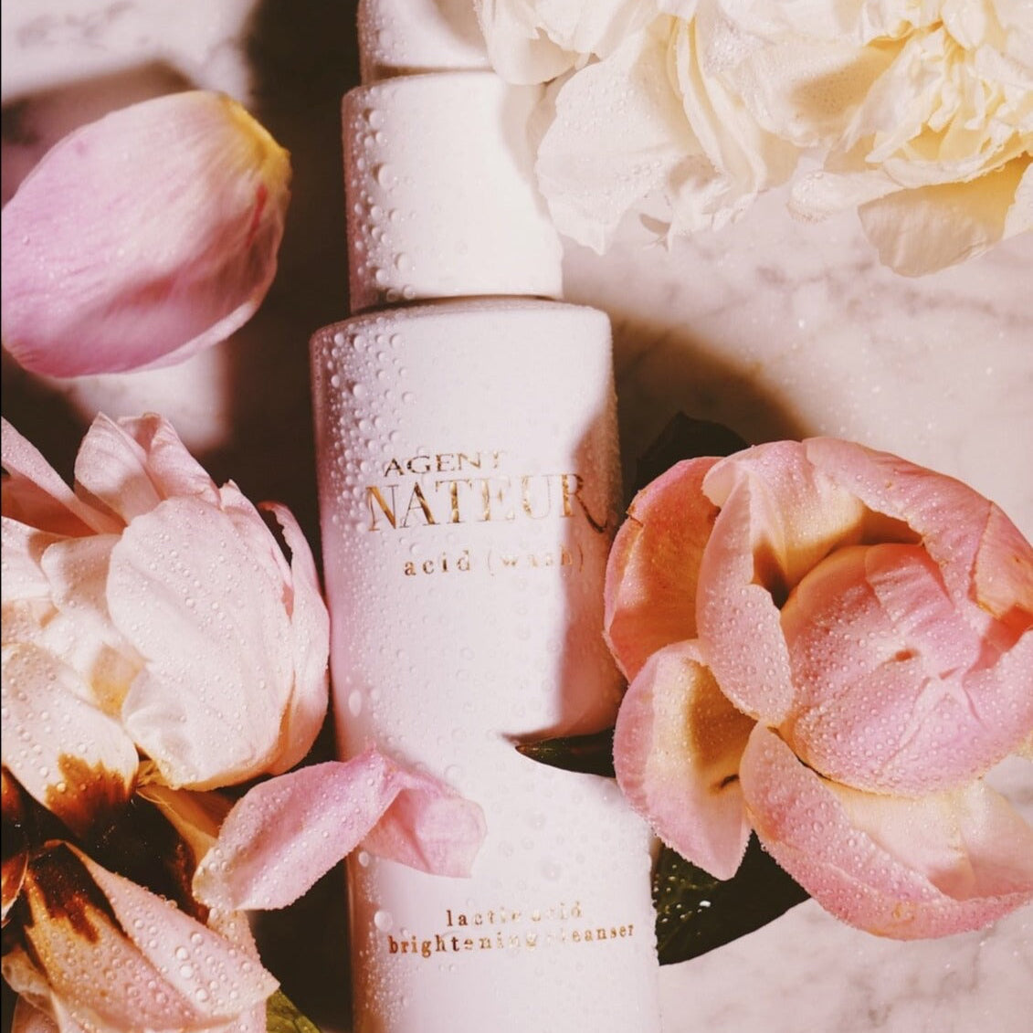 Agent Nateur Acid Wash Flasche auf weißem Marmortisch mit rosa Blüten