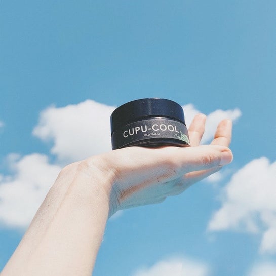 Frauenhand hält schwarzen Cupu Cool Tiegel vor blauen Himmel mit weißen Wolken