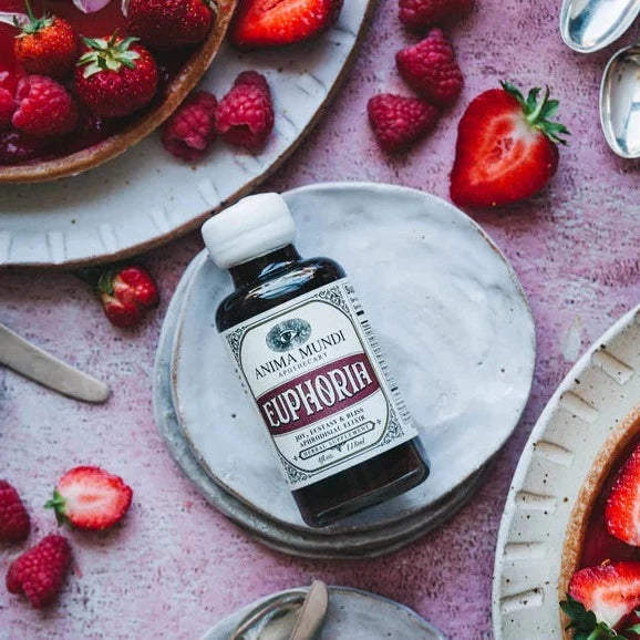 Anima Mundi Glasflasche Euphoria liegt auf einer Steinplatte dekortiert mit Erdbeeren und Himbeeren, aus der Vogelperspektive.