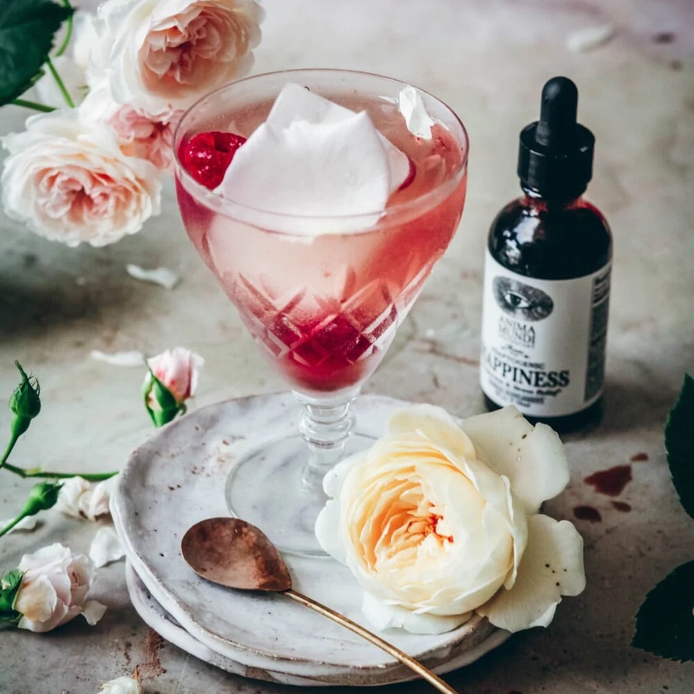 Anima Mundi Glaspipettenflasche Happiness steht neben einem Glas mit rosa Flüssigkeit und Beeren.