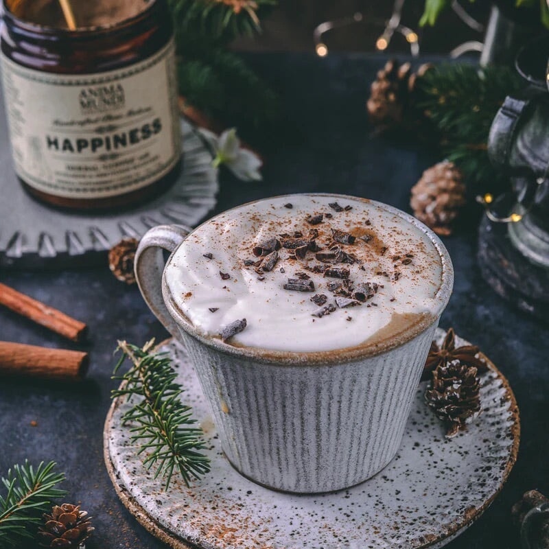 Mit Schokosplittern dekorierte Kaffeetasse, im Hintergrund ein Anima Mundi Happiness Schraublas.