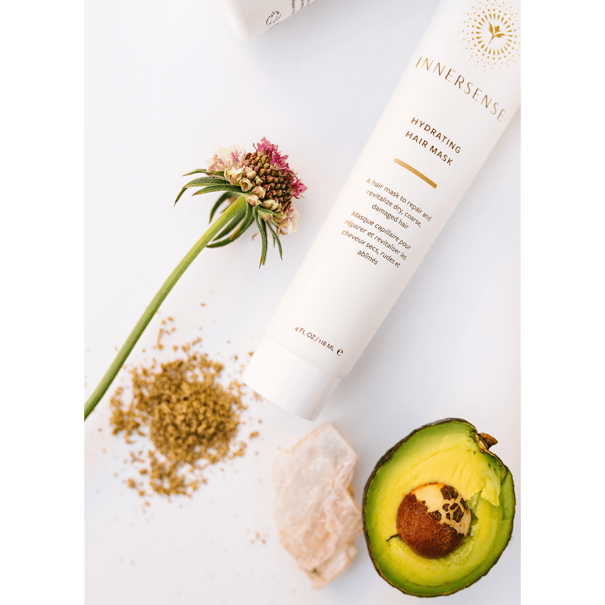 Innersense Hydrating Hair Mask Tube liegt neben einer Blume und einer aufgschnittenen Avocadohälfte.