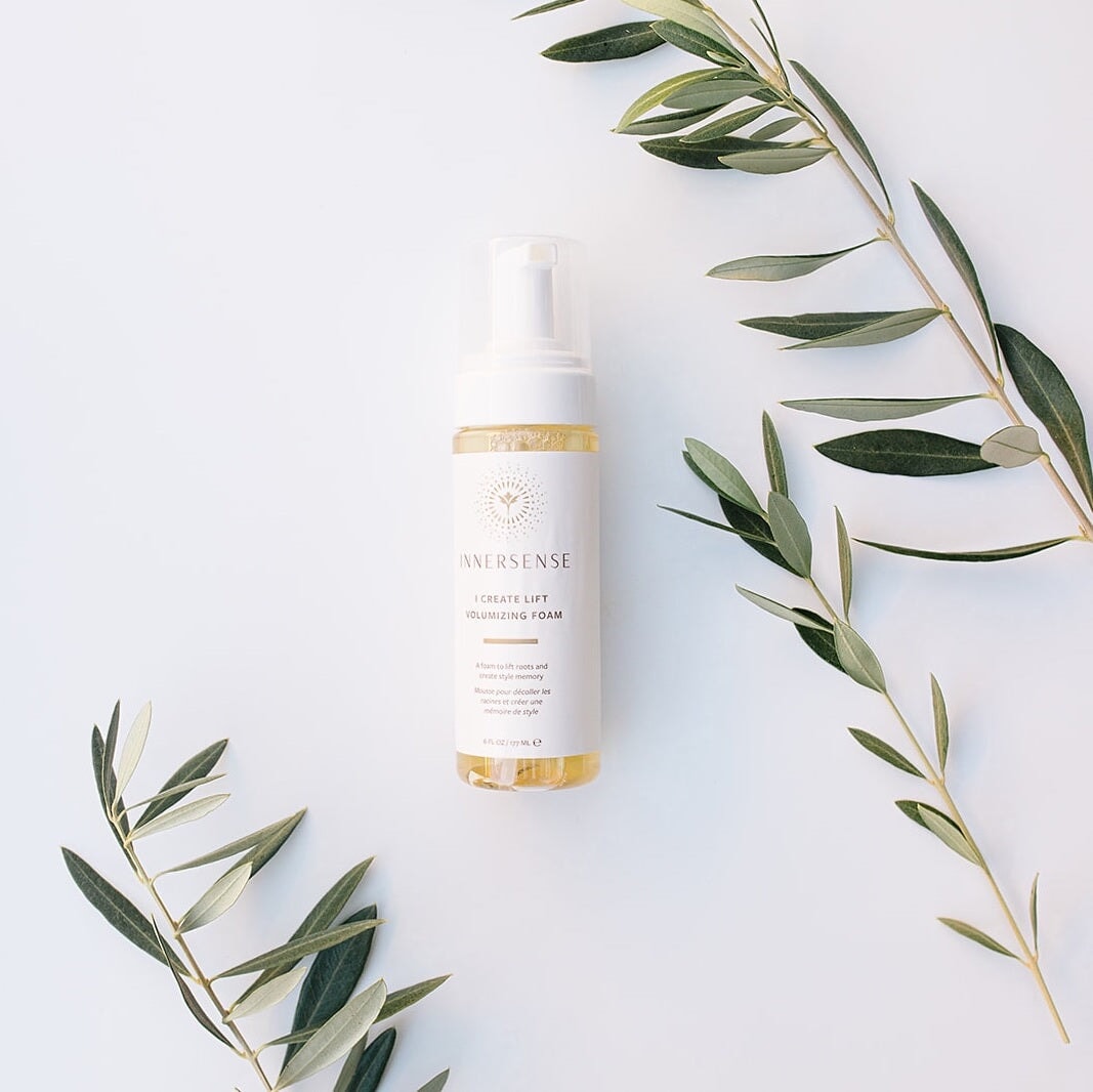 Zwischen 3 Olivenbaumzweigen liegt eine Sprühflasche Innersense I Create Lift Volumizing Foam auf weißem Hintergrund.