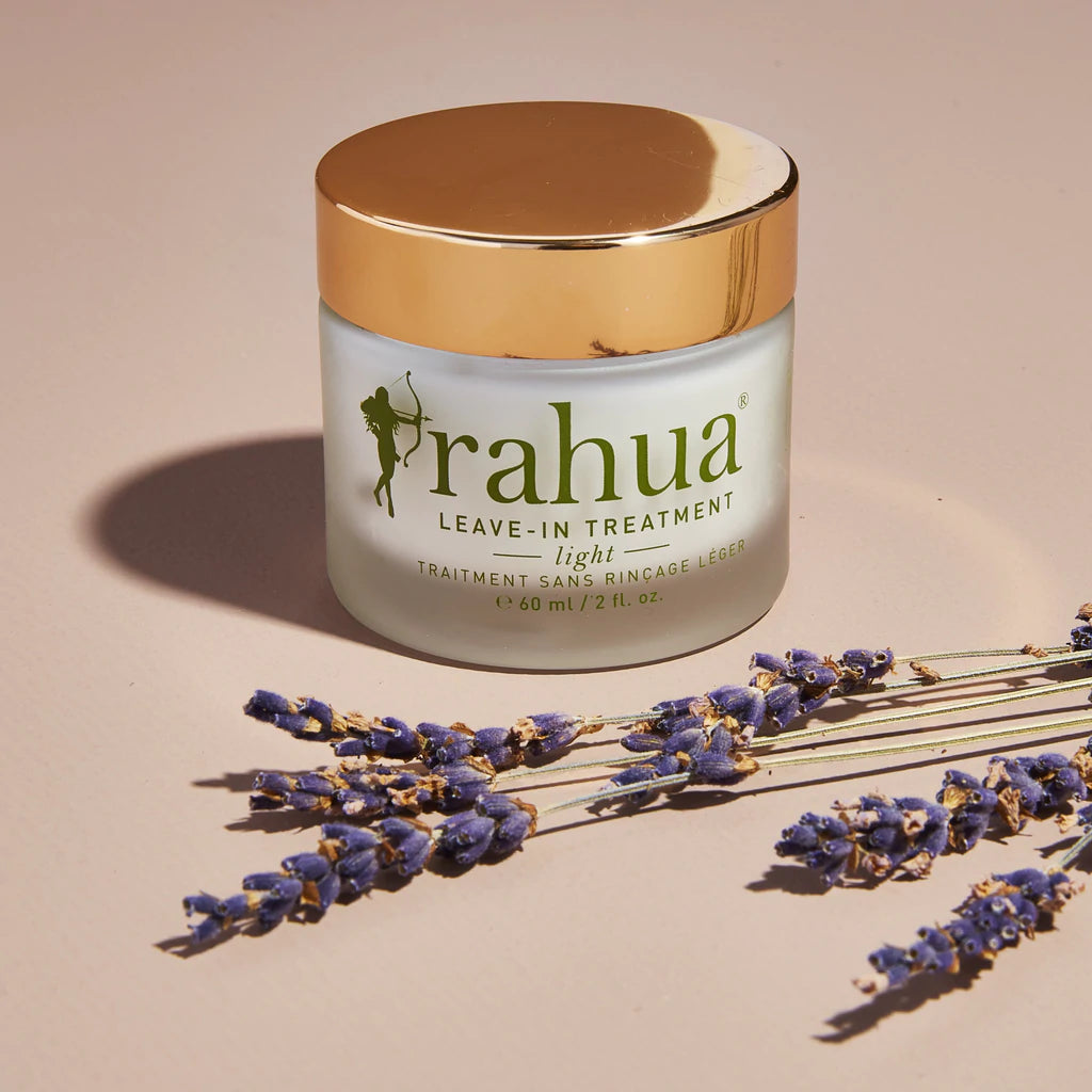 Rahua Leave-In Treatment Light Glas mit Schraubdeckel vor cremefarbenem Hintergrund dekoriert mit Lavendelblüten.