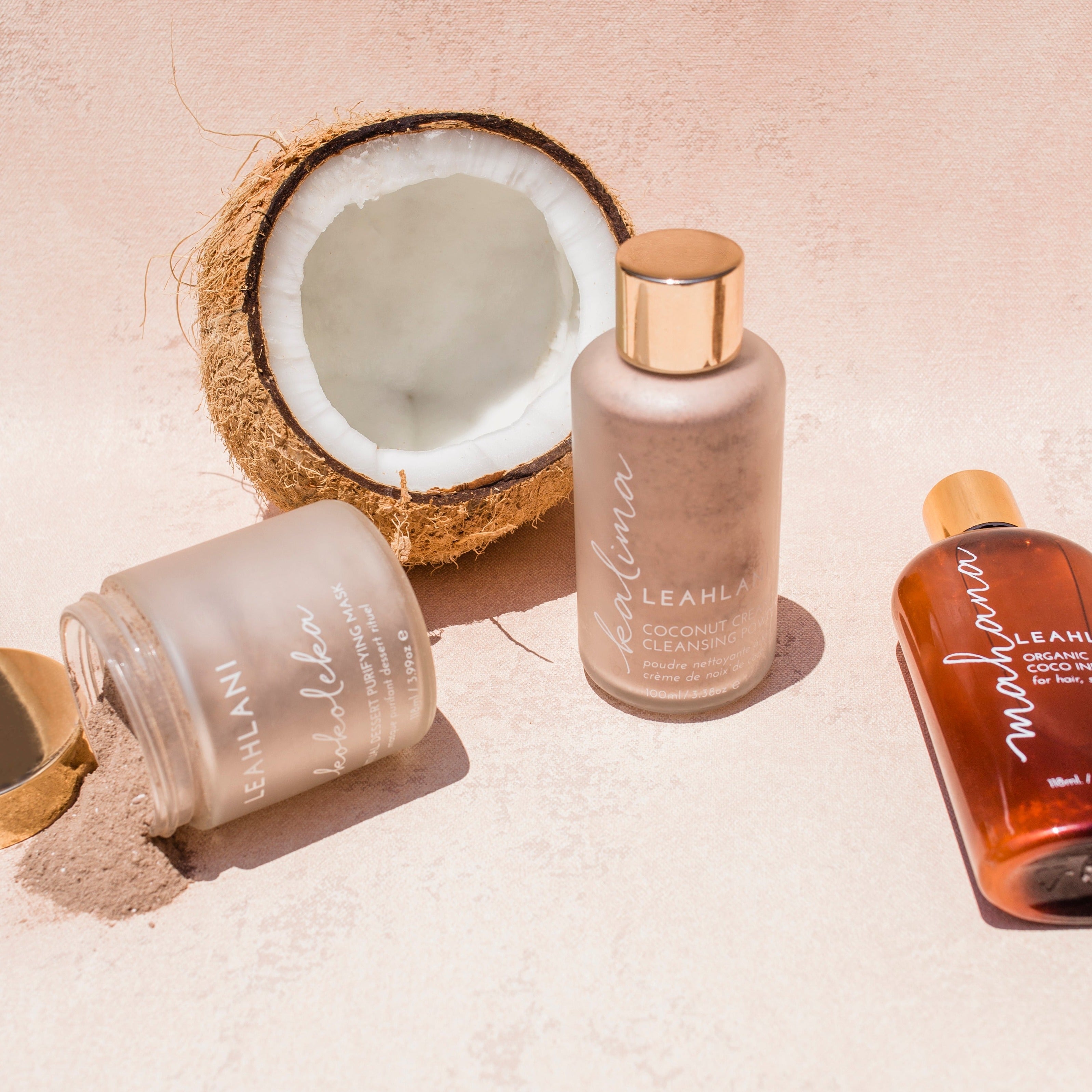 Leahlani Kalima Cleansing Powder Flakon mit Kokoleka Maske und Mahana Öl vor aufgeschnittener Kokosnuss