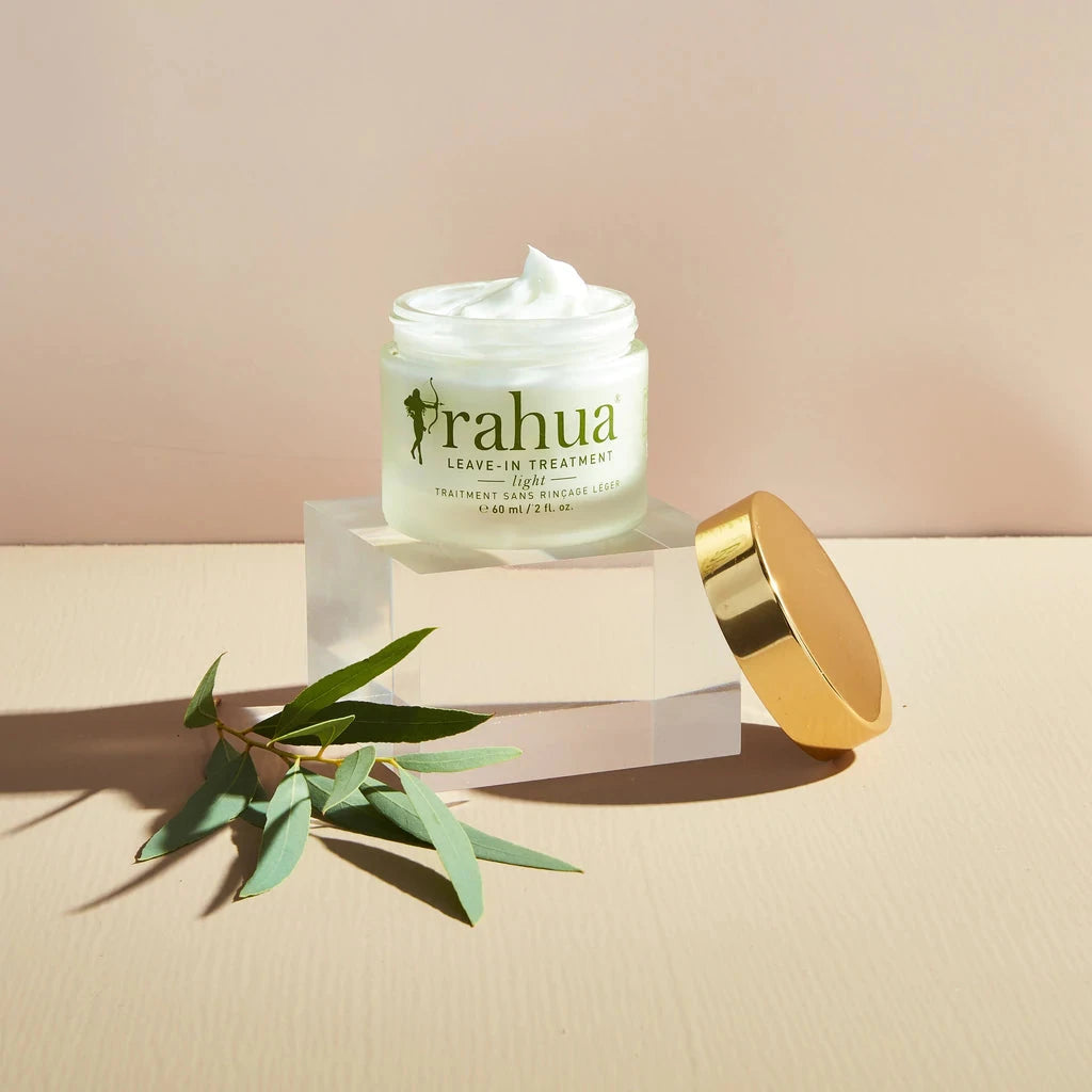 Rahua Leave-In Treatment Light Glas mit Schraubdeckel und Texturbeispiel vor cremefarbenem Hintergrund.
