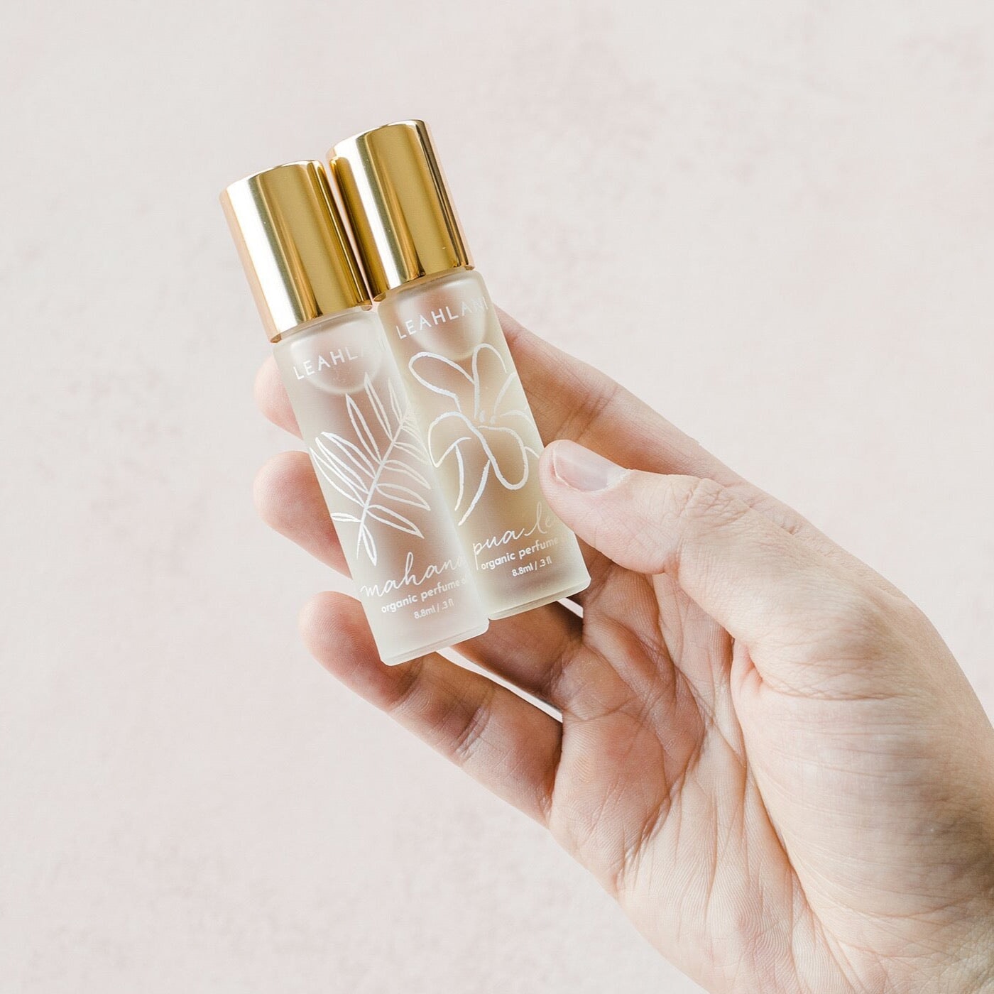 Leahlani Mahana Perfume Oil und Pua Lei wird von weiblicher Hand vor hellem Hintergrund gehalten