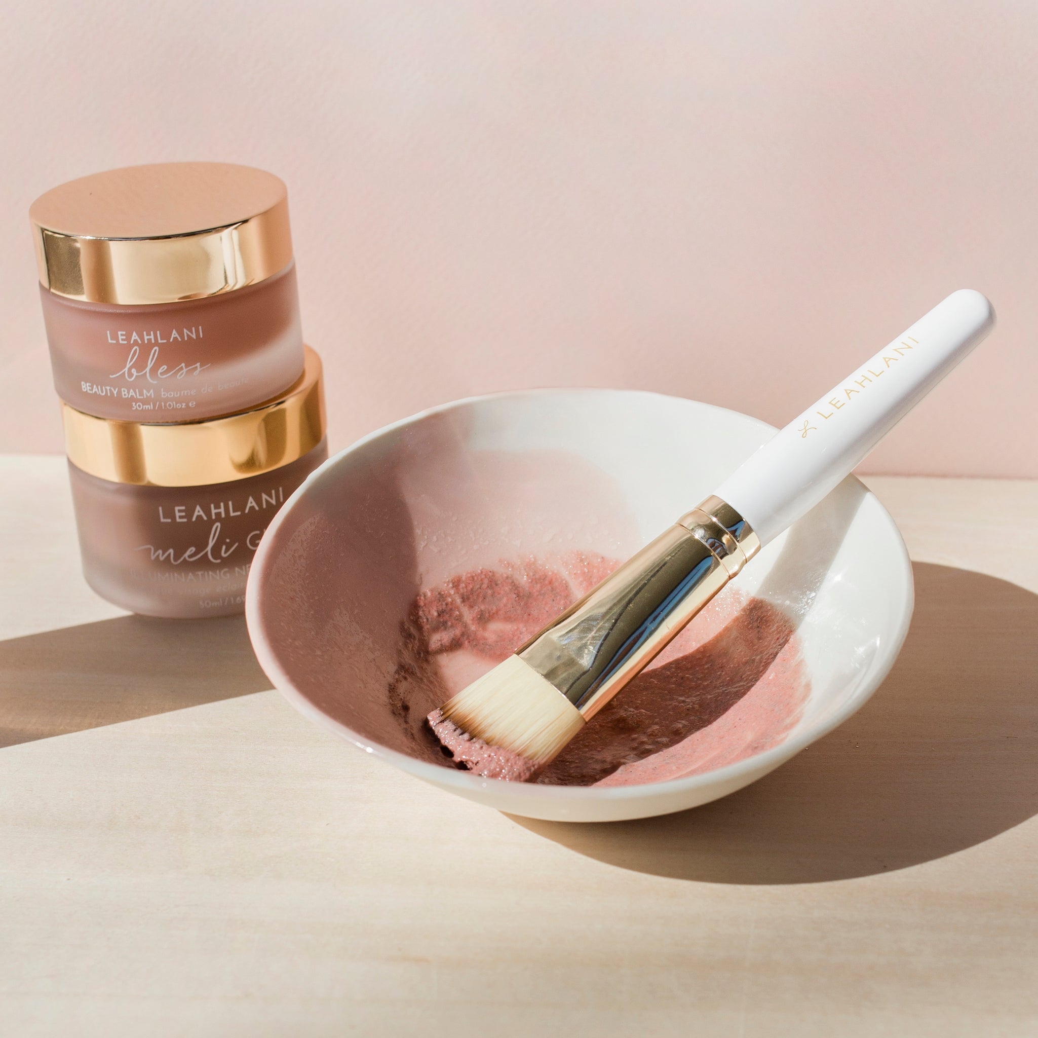 Leahlani Meli Glow Mask und Bless Balm gestapelt hinter weißer Schale mit Pinsel