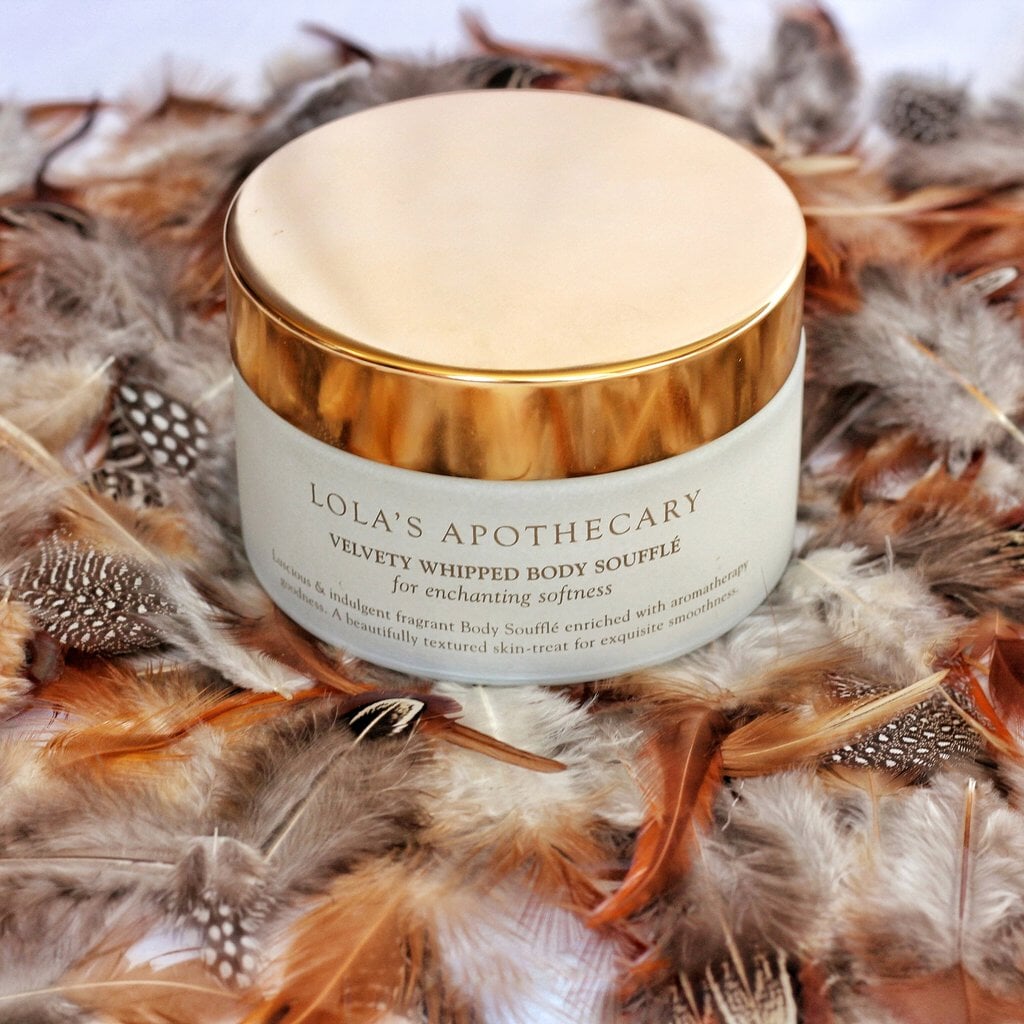 Lola's Apothecary Body Soufflé Tiegel mit goldenem Deckel steht auf Federn.