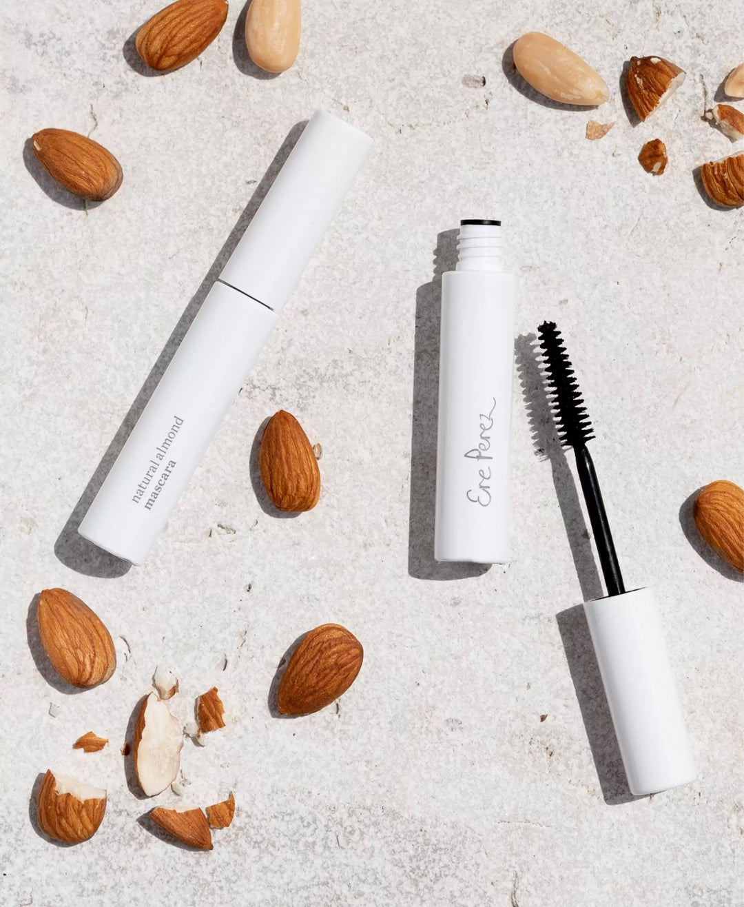Wimpernbürste und geschlossene Ere Perez Natural Almond Mascara liegt zwischen Mandeln auf weißem Untergrund.