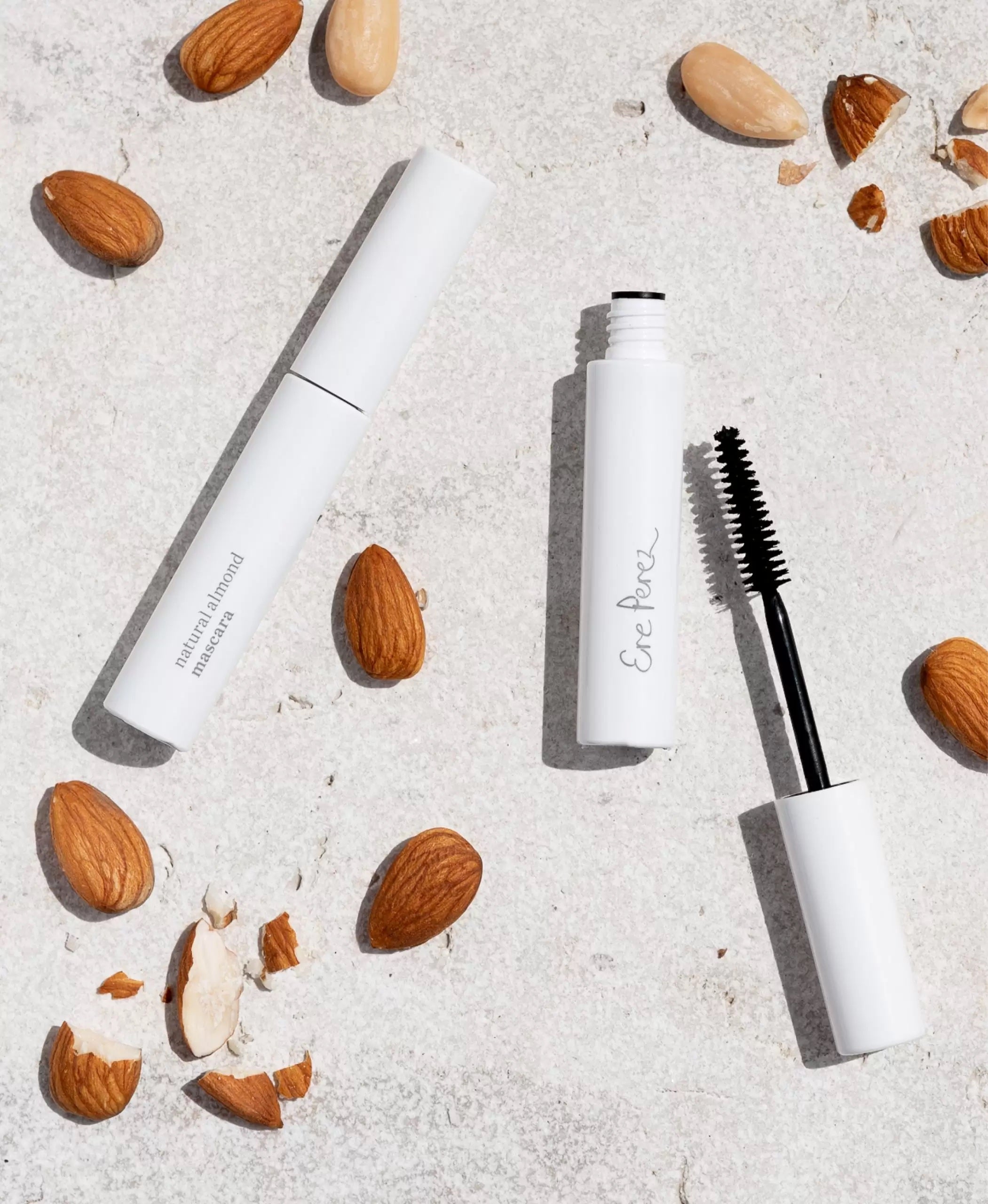 Wimpernbürste und geschlossene Ere Perez Natural Almond Mascara liegt zwischen Mandeln auf weißem Untergrund.