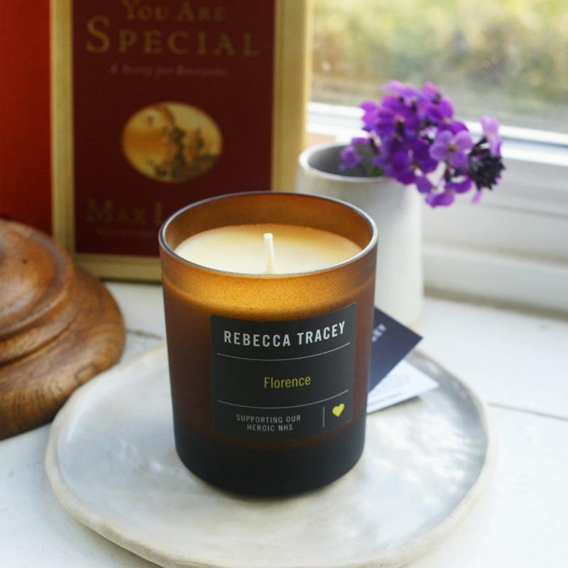 Kerze "Florence" von Rebecca Tracey stehend auf einem Teller, umgeben von einem Buch und einer kleines Vase mit Blumen.