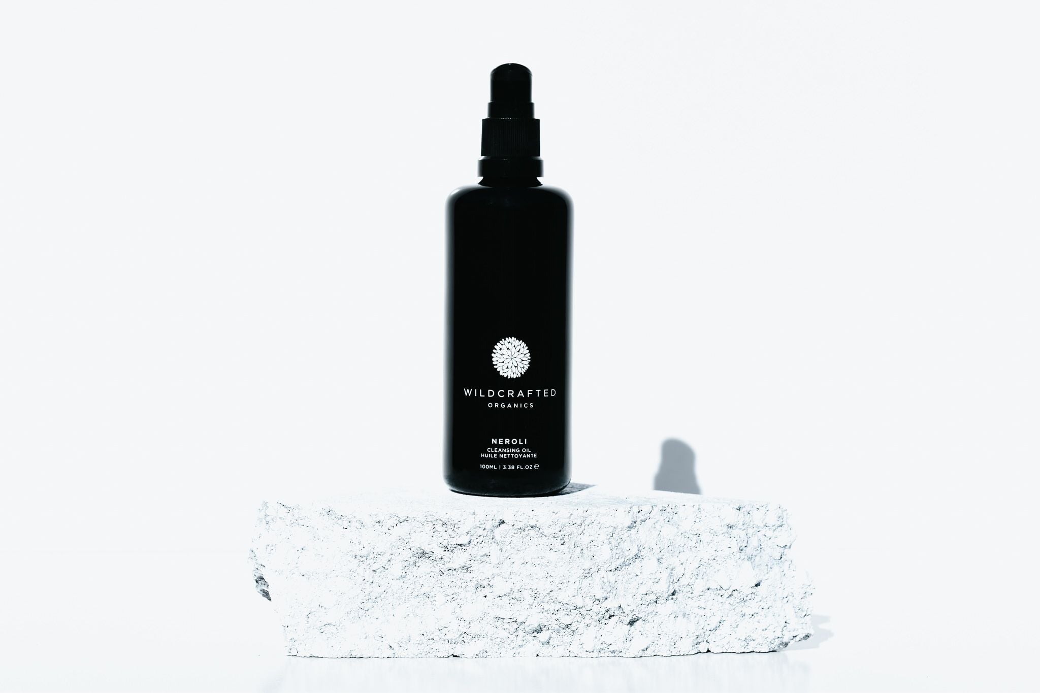 Schwarze Pumpflasche von Wildcrafted Organics Neroli Cleanser steht auf einer hellen Steinplatte.
