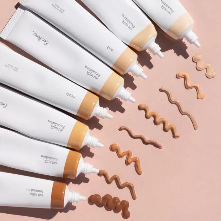 7 offene Tuben Oat Milk Foundation von Ere Perez jeweils mit Textur- und Farbbeispielen im Zickzackmuster.