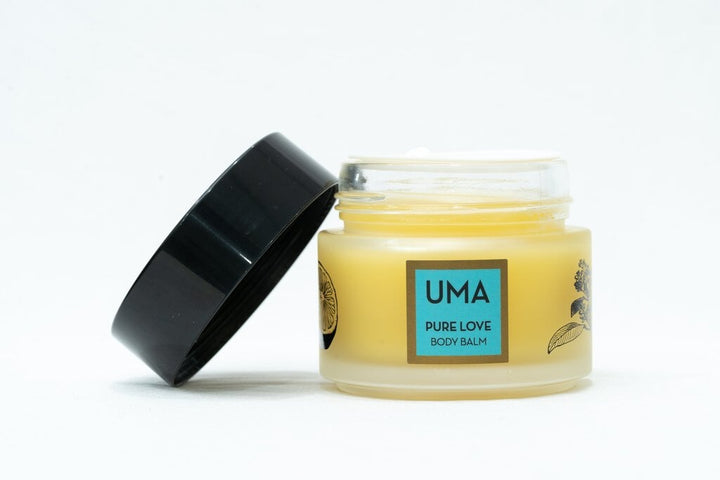 Schraubglas UMA Pure Love Body Balm mit offenem, schräg an das Glas angelehnten schwarzem Deckel steht vor weißem Hintergrund.