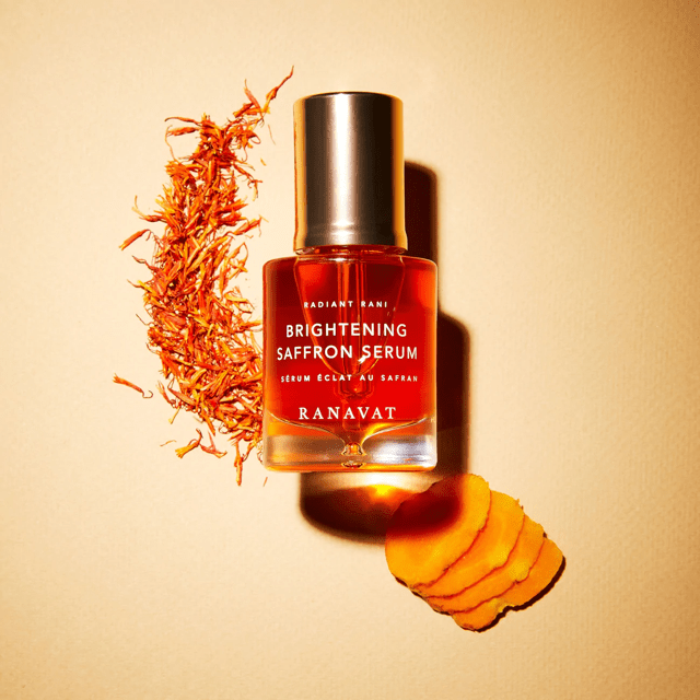 Ranavat Radiant Rani Brightening Saffron Serum Flasche auf orangen Hintergrund mit Safran Fäden und Wurzeln
