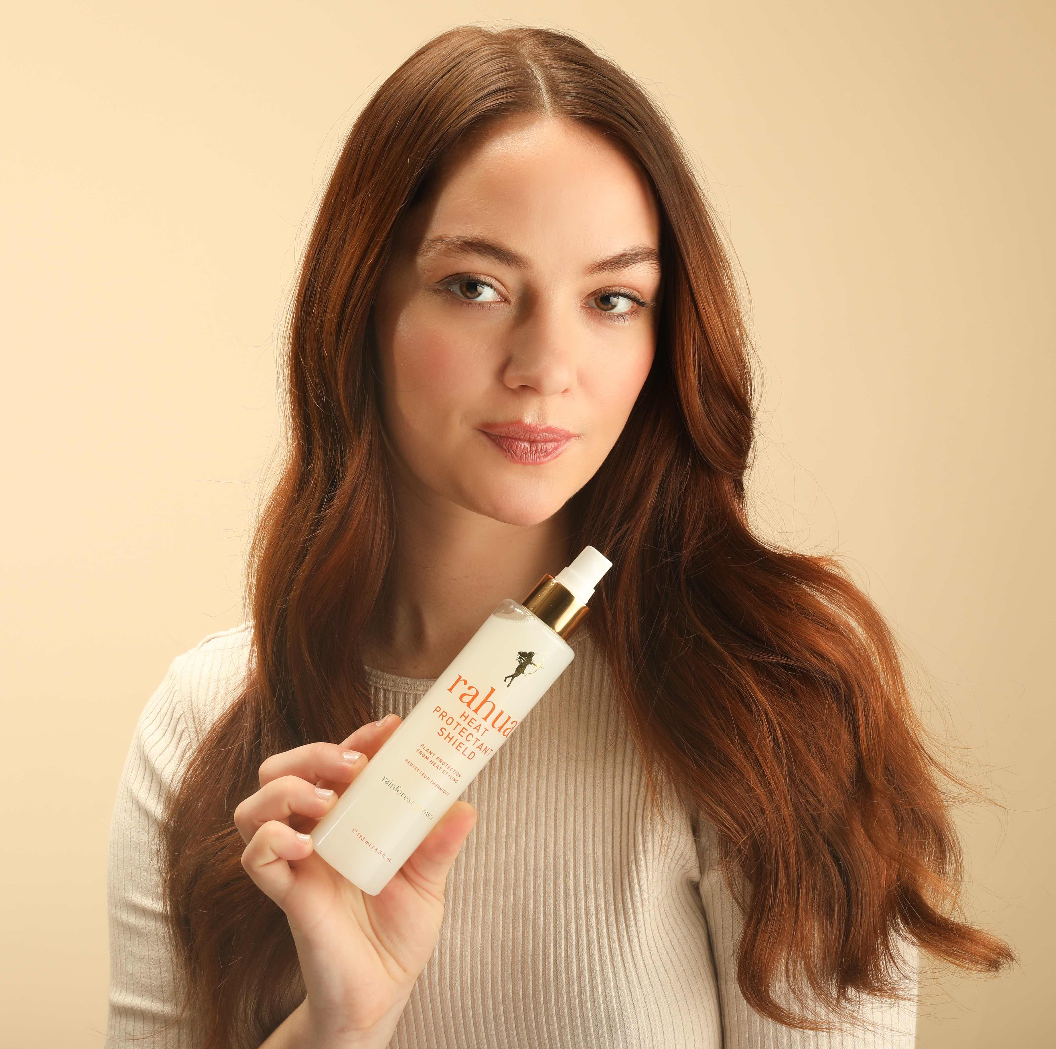 Brünette Frau hält eine Flasche Rahua Heat Protection Shield Flasche in der Hand.