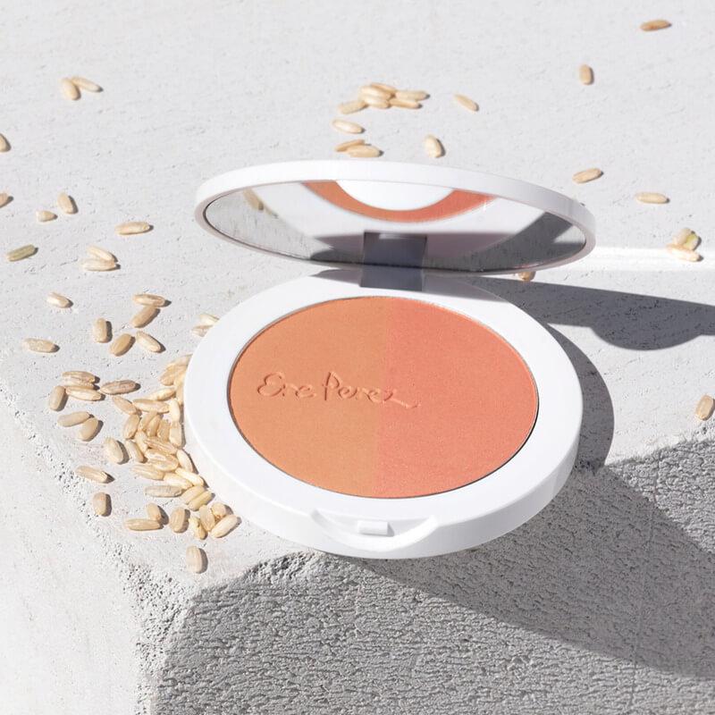 Offene Dose des Rice Powder Blush & Bronzer BROOKLYN auf hellem Untergrund mit Reiskörnern.