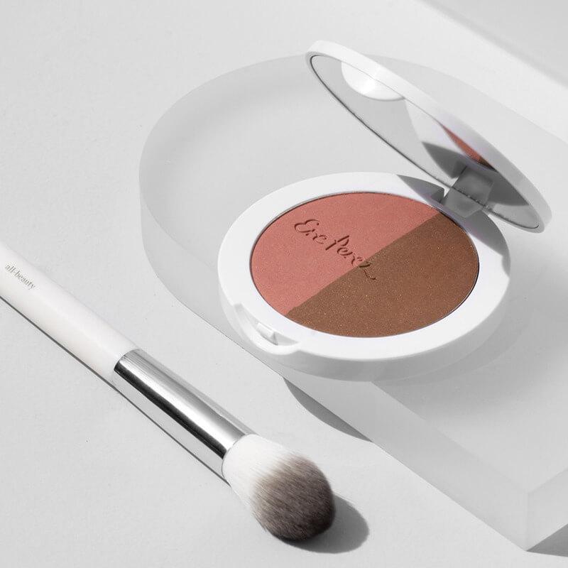 Offene Dose Rice Powder Blush & Bronzer BROOKLYN liegt neben einem Pinsel auf hellem Untergrund.