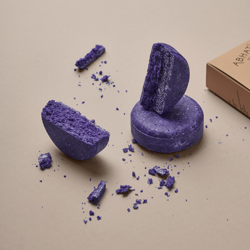 Abhati Suisse Sattal fester Conditioner liegt halbiert auf einem ganzen Stück, im Hintergrund die Verpackung.