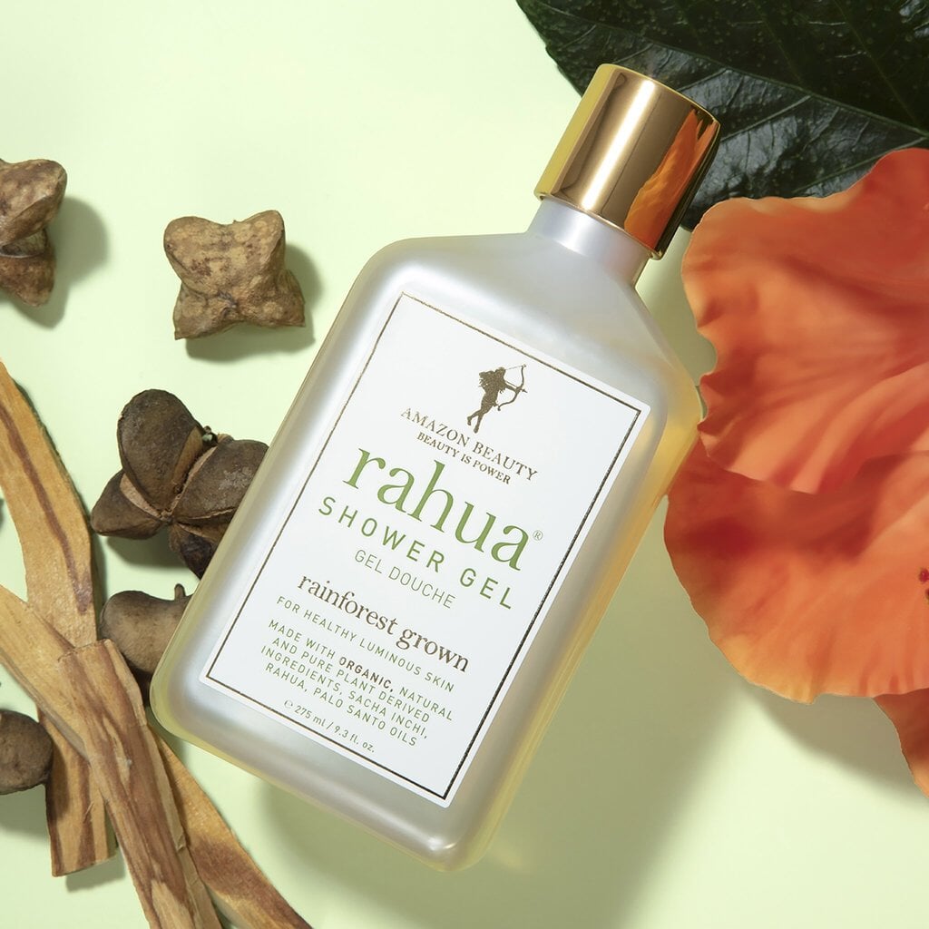 Rahua Shower Gel Flasche vor hellgrünem Hintergrund dekoriert mit Palo Santo und Blütenblättern.