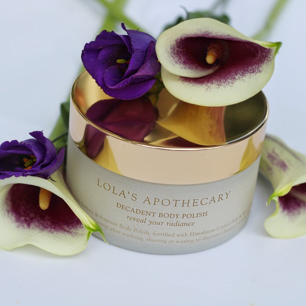 Lola's Apothecary Glastiegel Body Polish mit goldenem Deckel geschmückt mit verschiedenen Blumen, steht auf weißem Untergrund.
