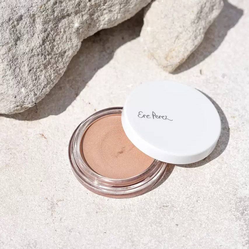 Offener Tiegel Ere Perez Vanilla Highlighter liegt im Sand zwischen Steinen.