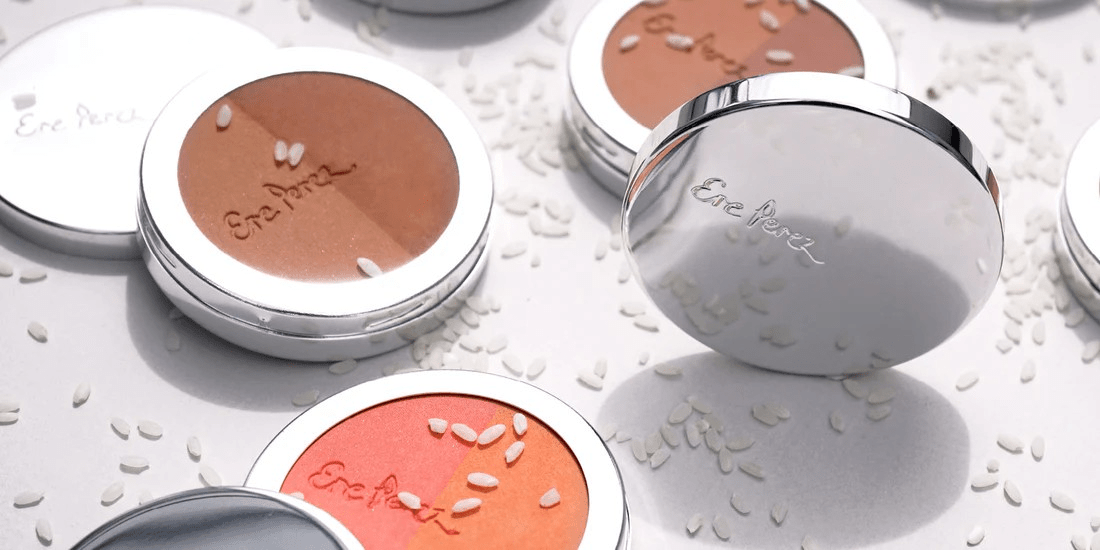 Various bronzers and blushes by Ere Perez lie open on a white background with scattered grains of rice.