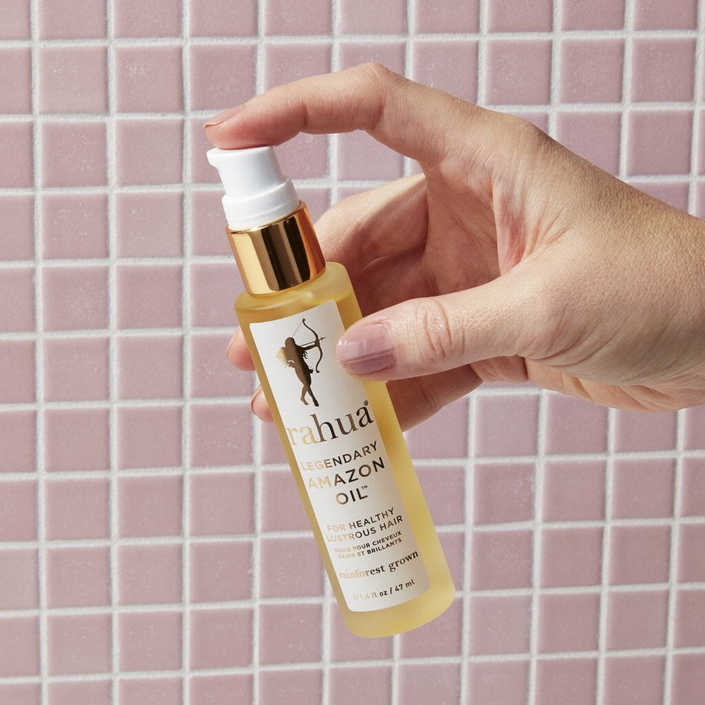 Rahua Legendary Amazon Oil bottle held by a hand in front of a pink tile background.