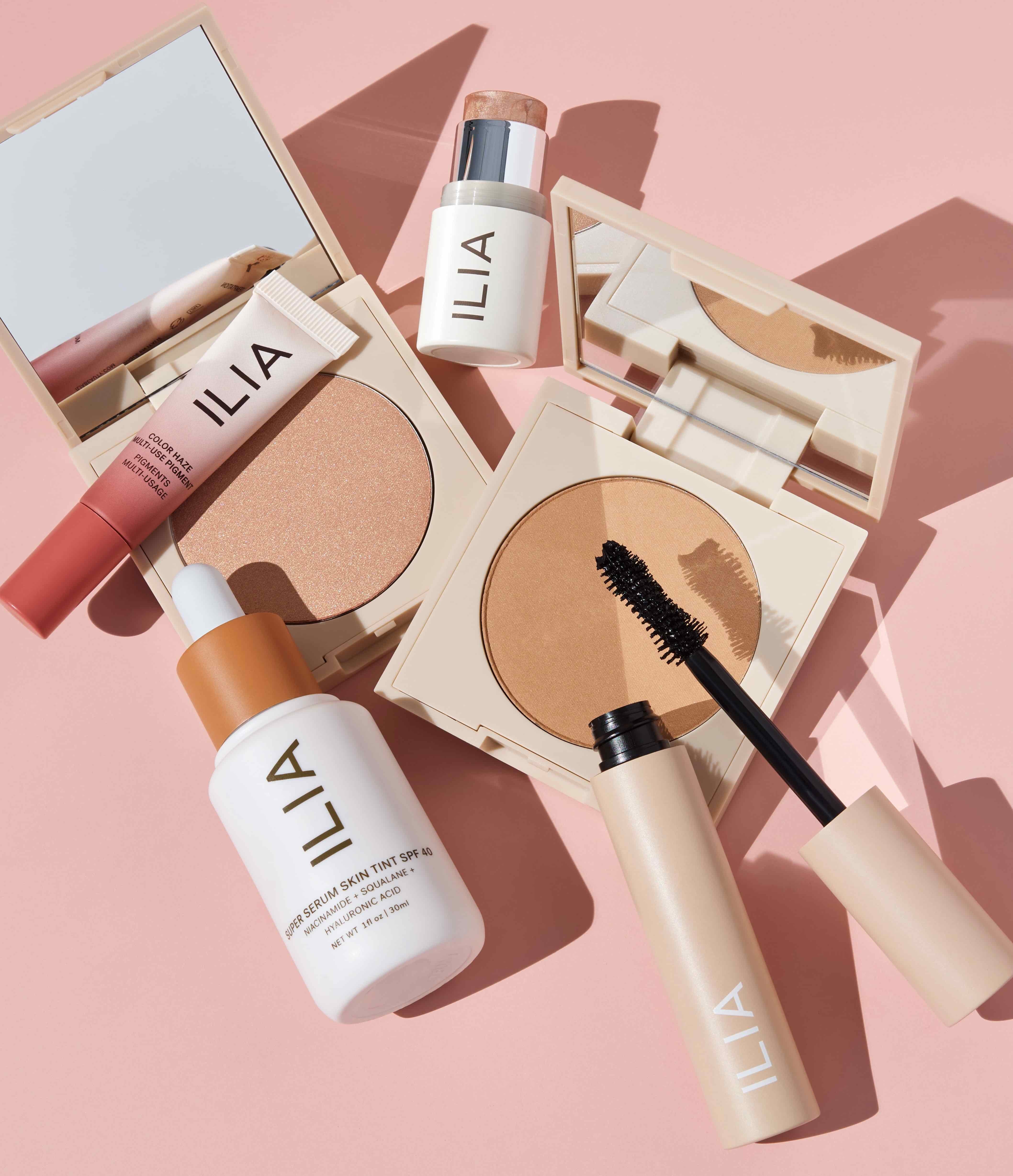 Verschieden ILIA Beauty Produkte liegen verteilt auf rosafarbenem Untergrund.