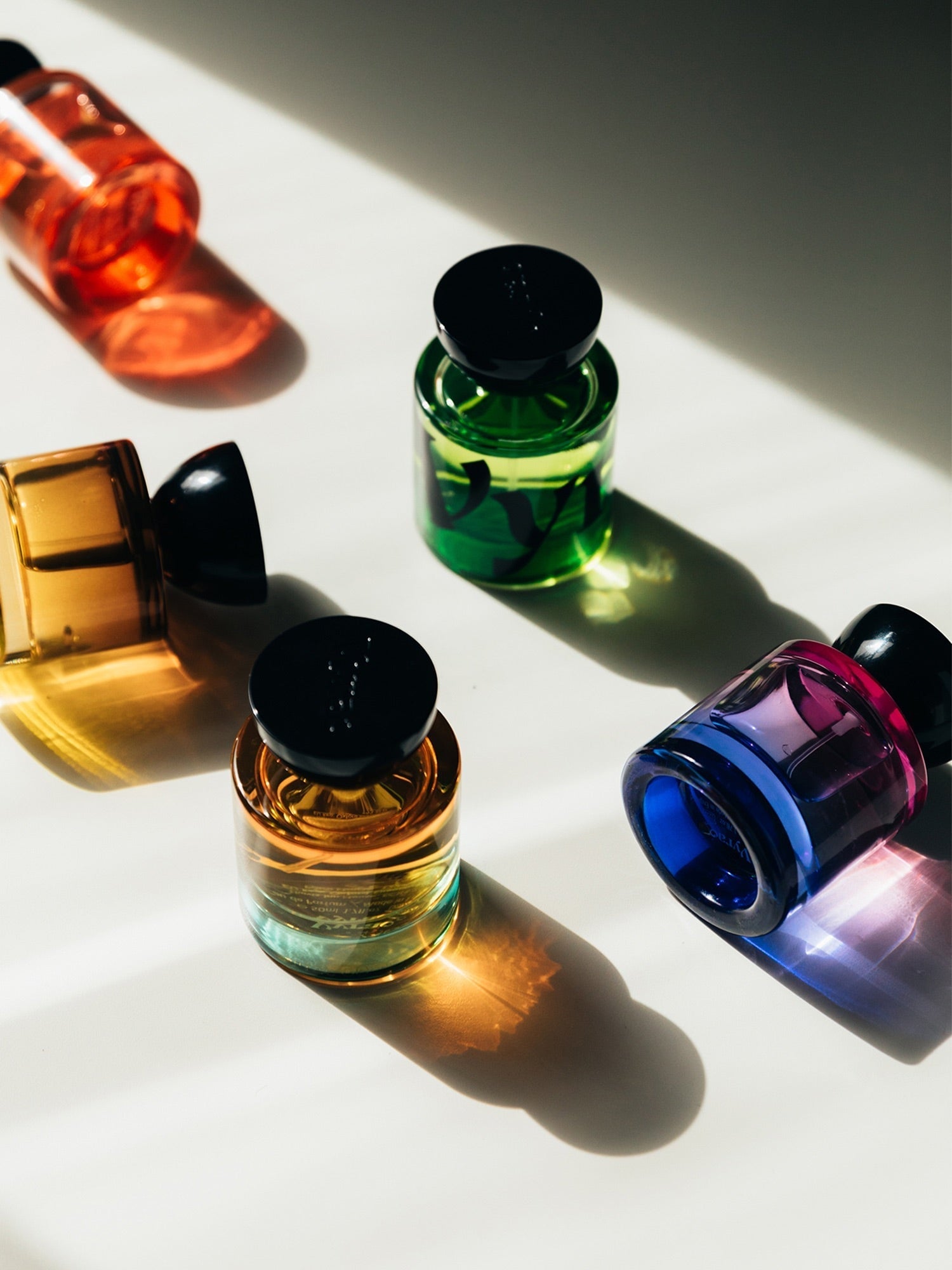 Verschieden bunte Glasflakons von Vyrao liegen und stehen auf hellem Untergrund.