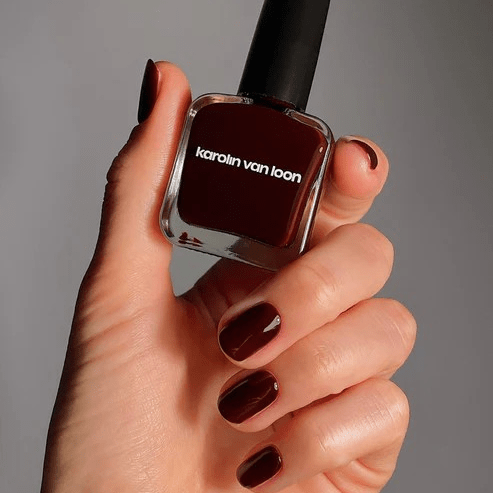 Gepflegte Hand hält eine 15-ml-Flasche roter Nagellack Rouge Royale von Karolin Van Loon – vegan & luxuriös