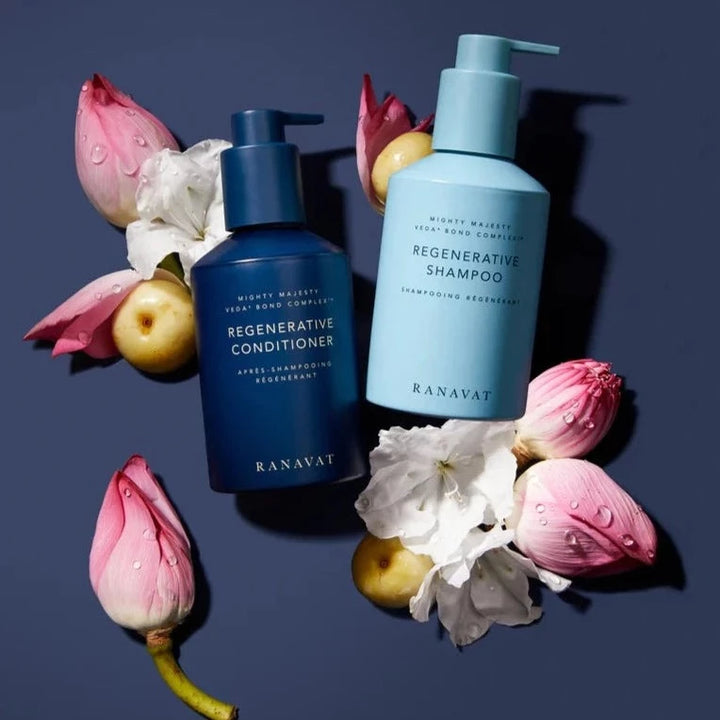 Regenerative Conditioner und Shampoo Flaschen auf blauem Hintergrund mit rosa Blüten und gelben Früchten