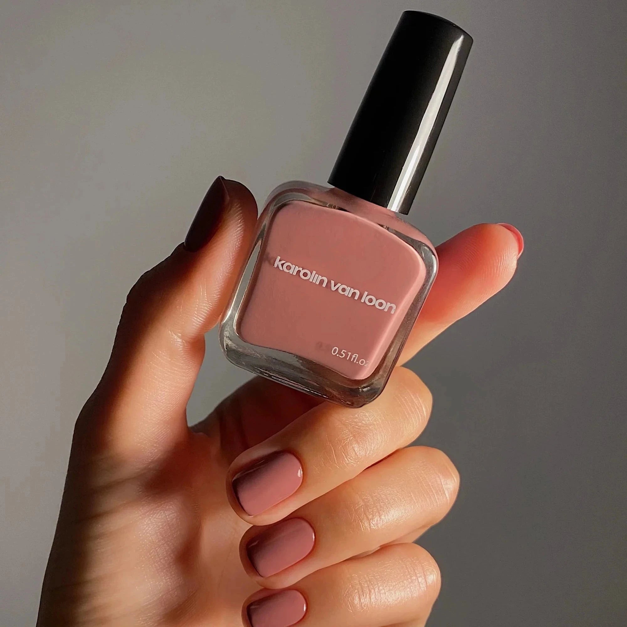 Karolin Van Loon – 55 Blush de Satin Nagellack in einer Hand mit lackierten Nägeln.