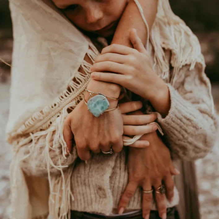 Arme, die ein Kind umarmen, wobei ein Arm einen Larimar Armreif mit türkisfarbenem Edelstein trägt. North Glow