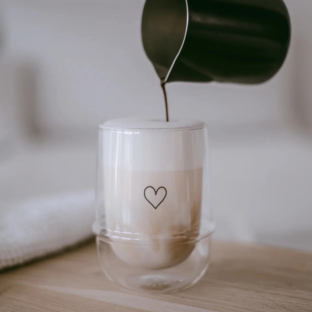 Doppelwandiges Latte Machiato Glas mit Herz von eulenschnitt wird von einer kleinen Kanne mit Kaffee befüllt. North Glow