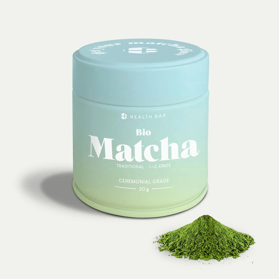 Bio Matcha on Health Bar, blau grüne Verpackung vor hellem Hintergrund, daneben grünes Matchapulver. North Glow